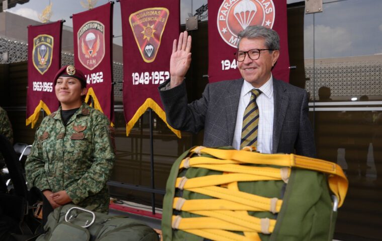 Ricardo Monreal saluda junto a una militar y equipo de paracaidismo durante una exhibición.